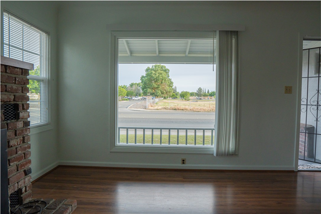 Empty living room with a brick fireplace, wood floors, and a large window overlooking the street.