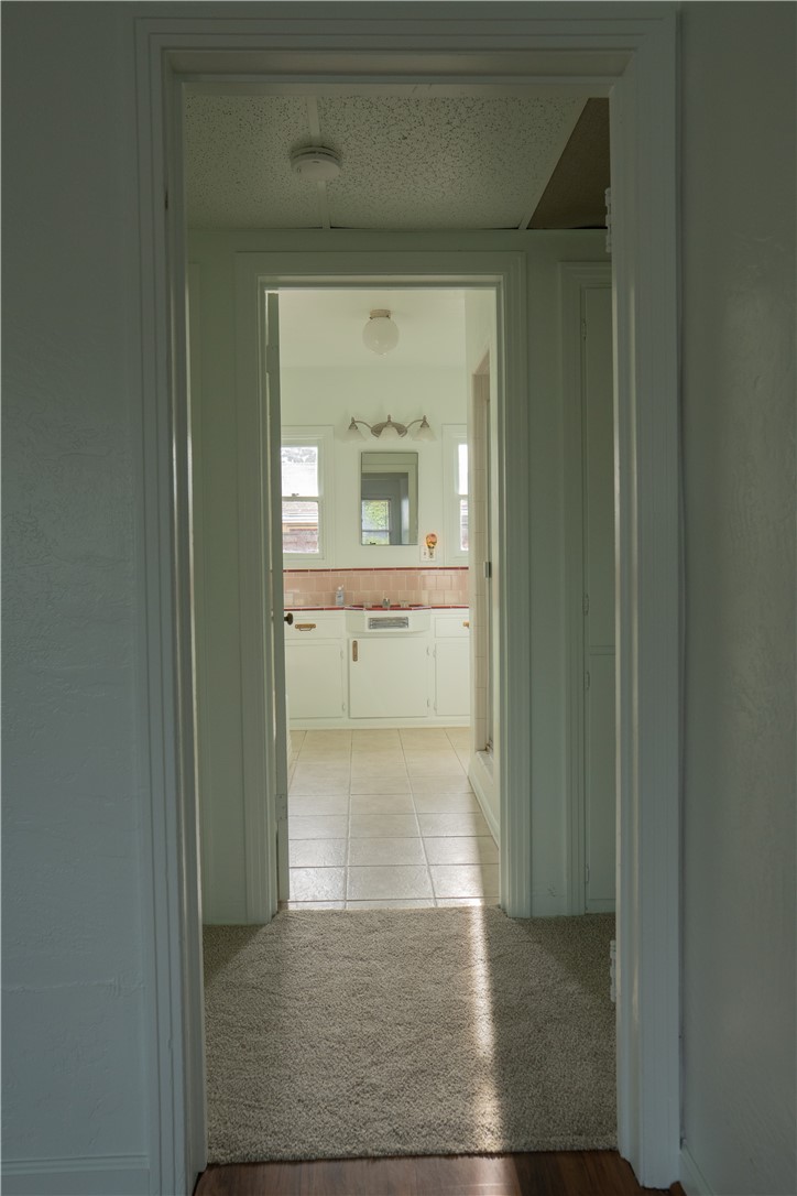 Hallway leading into a bright bathroom with white cabinetry and a red tile accent stripe.