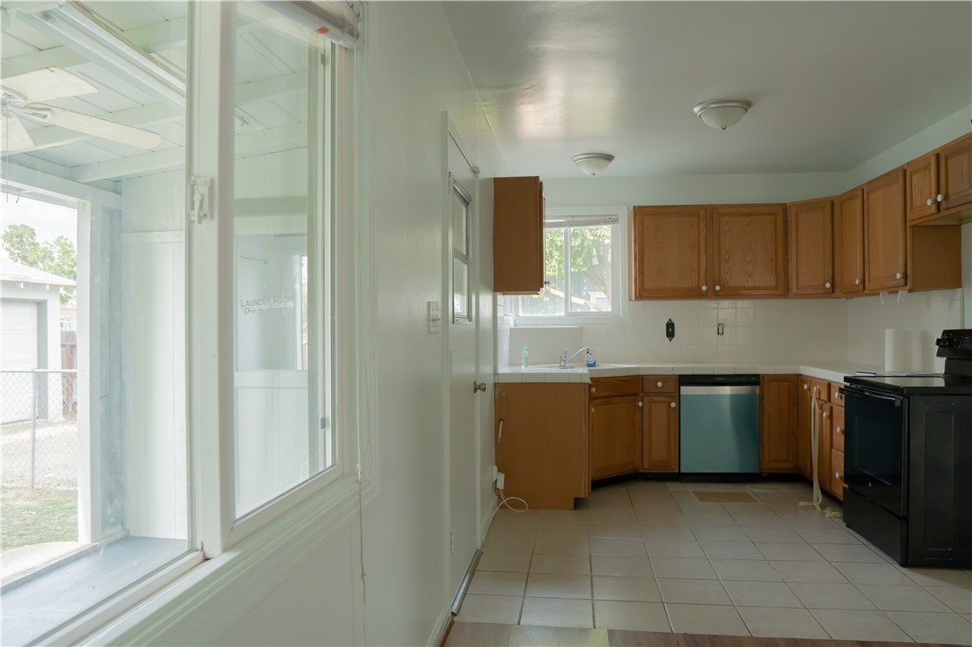 Vacant kitchen with wood cabinets, tiled floors, and a black range beside large windows.