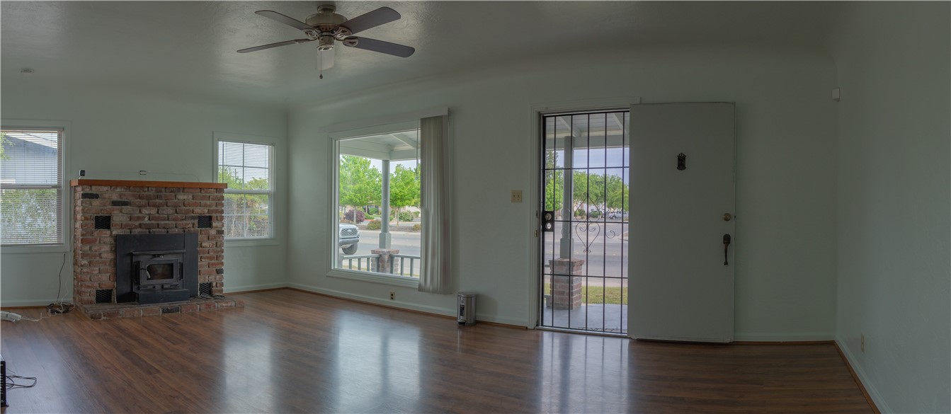 Empty living room with a brick fireplace, wood-look floors, and a front door with a metal security gate.