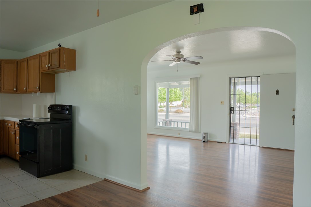 Empty kitchen with wood cabinets and black range, opening into a bright living room.