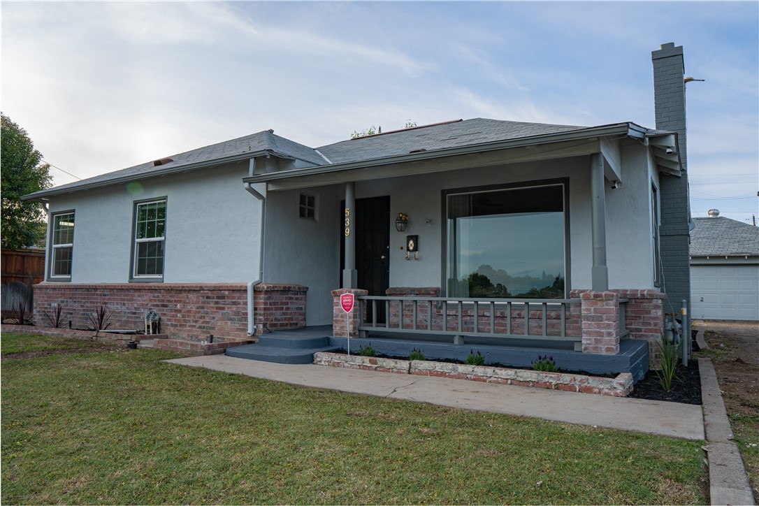 Gray single-story home with brick porch trim, a broad front window, and a small lawn.