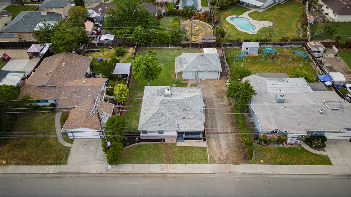 Aerial view of a single-story home with a light roof, front lawn, and long driveway.