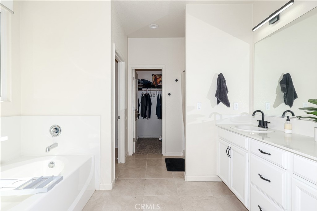 Primary bathroom with a soaking tub, white double vanity, and doorway to a walk-in closet.