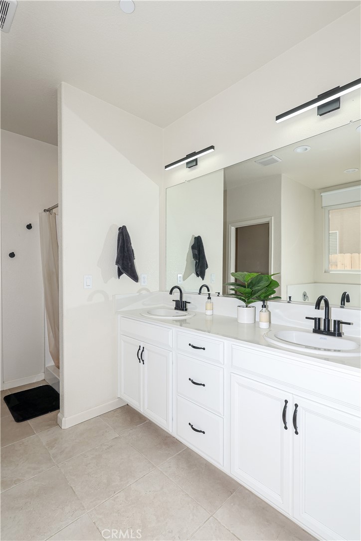 Bathroom with a white double-sink vanity, black faucets, large mirrors, and a shower at left.