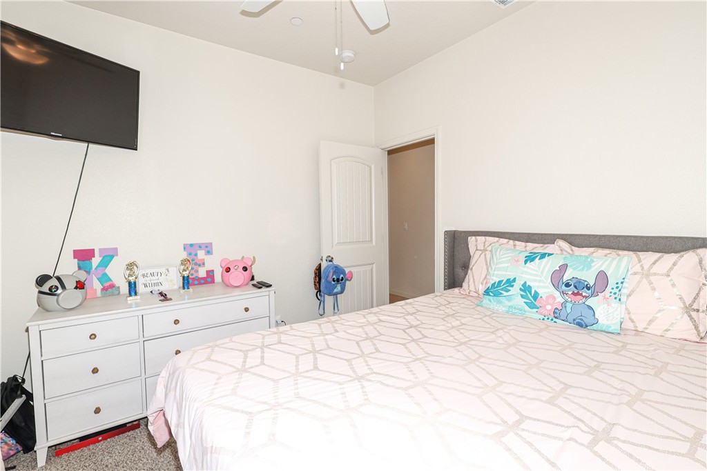 Bedroom with a geometric-patterned bedspread, gray upholstered headboard, white dresser, and wall-mounted television.