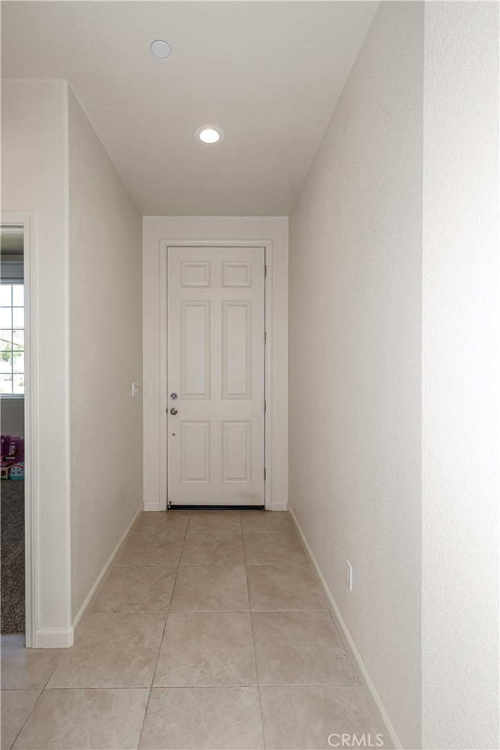 Entry hall with beige tile flooring leading to a white paneled front door.