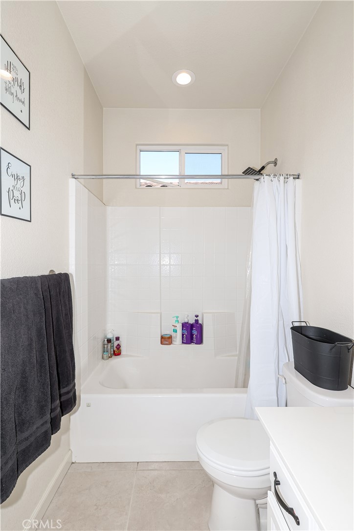 Bathroom with a white tiled tub and shower beneath a small high window.