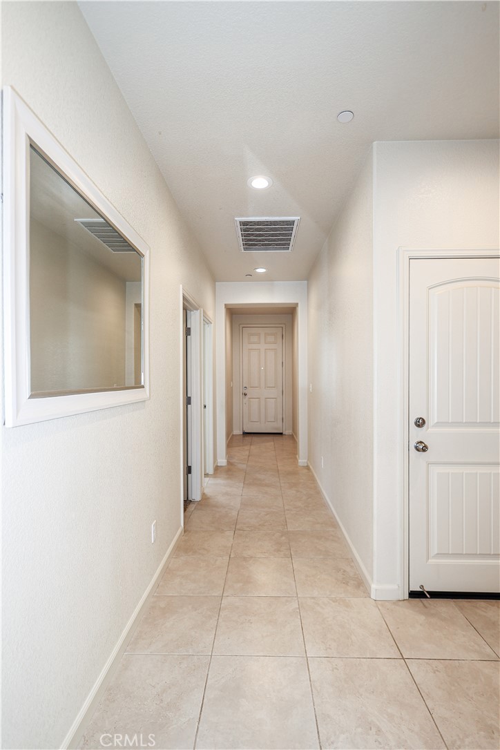 Unfurnished hallway with beige tile floors, a large wall mirror, and paneled doors.