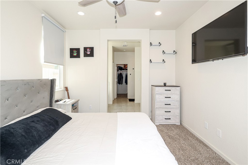 Furnished bedroom with a gray tufted headboard, wall-mounted television, and dresser.