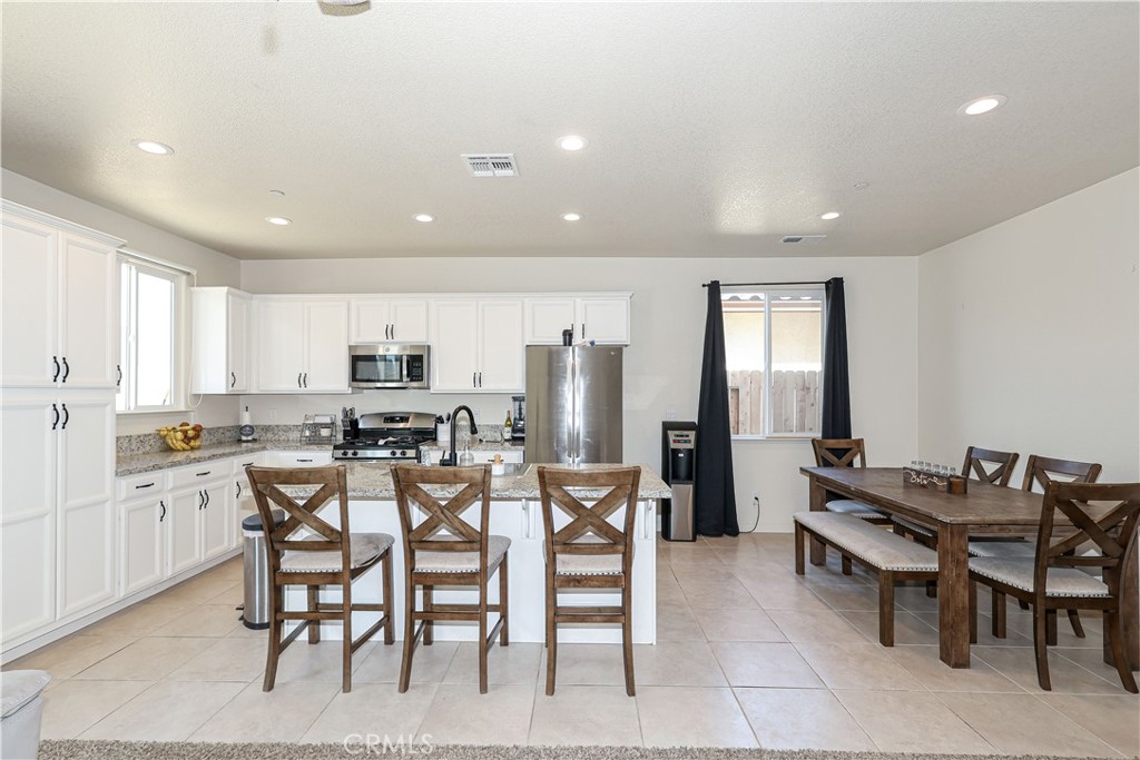 Kitchen and dining area with a granite island, white cabinets, stainless appliances, and a wood dining table.