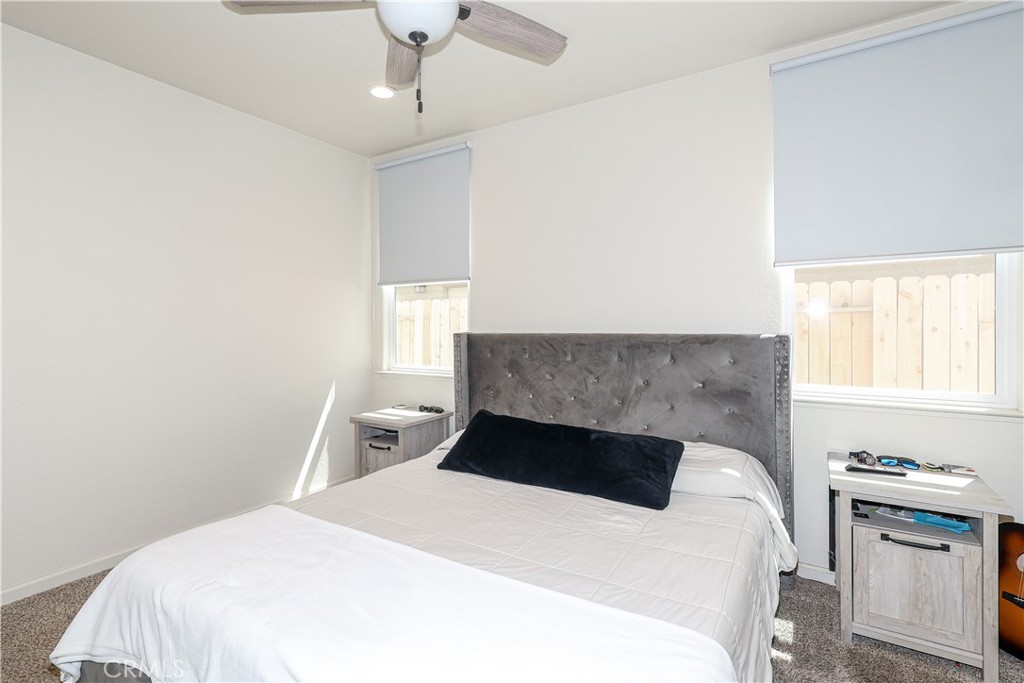 Bedroom with a white bed, gray tufted headboard, and roller shades over two windows.