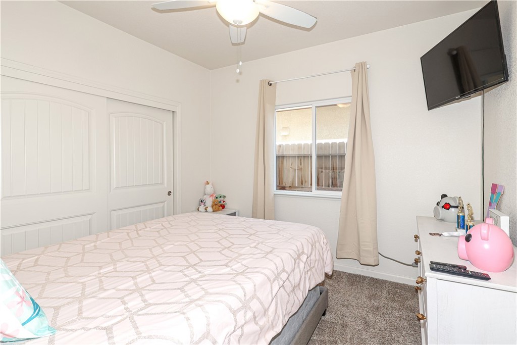 Furnished bedroom with a pale geometric quilt, white paneled closet doors, and wall-mounted television.