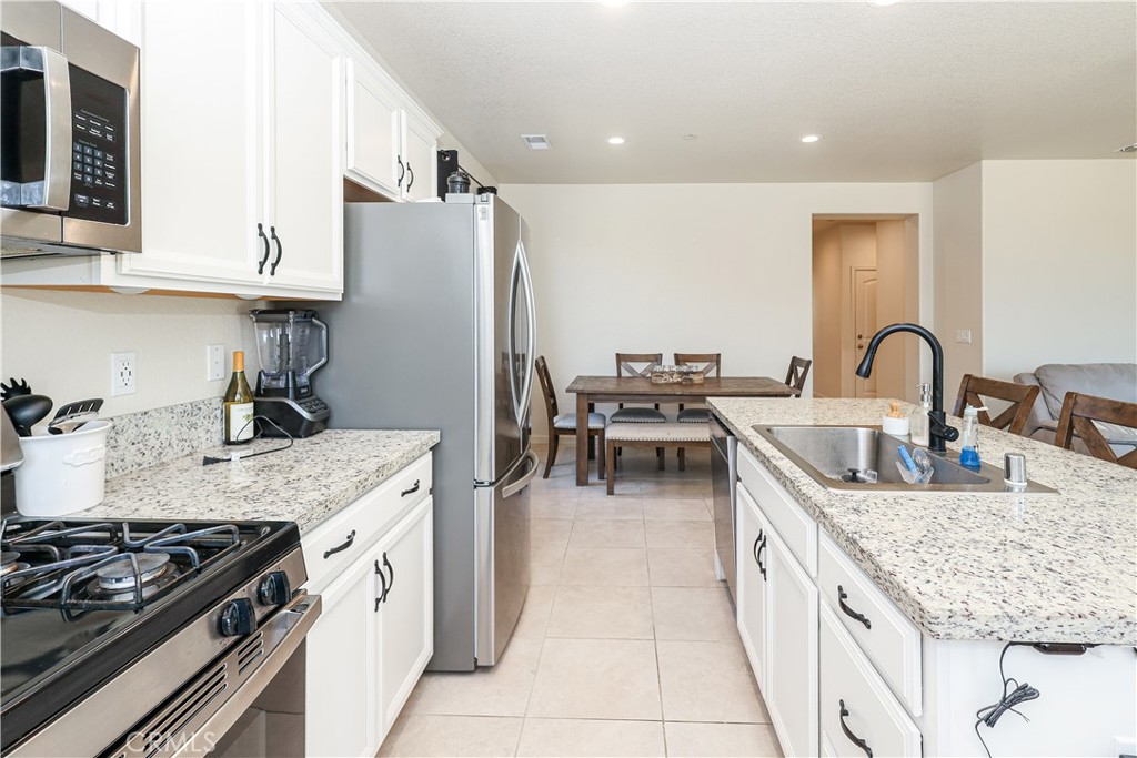Kitchen with white cabinets, stainless steel appliances, and a granite island with a sink.