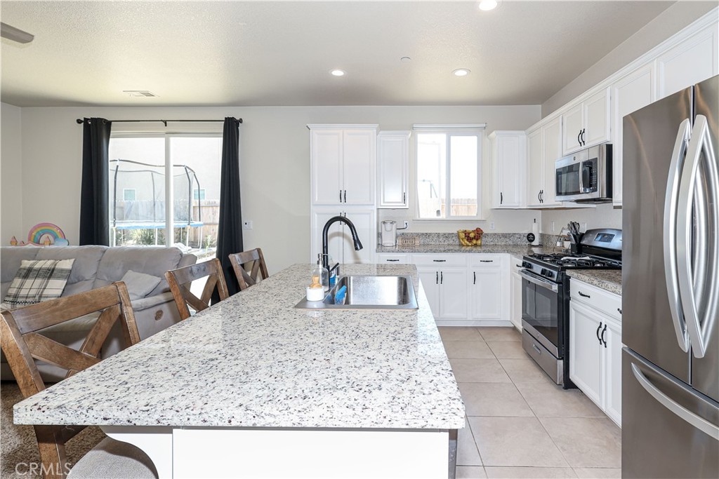 Bright kitchen with a granite island sink, white cabinets, and stainless steel appliances, opening to the living area.