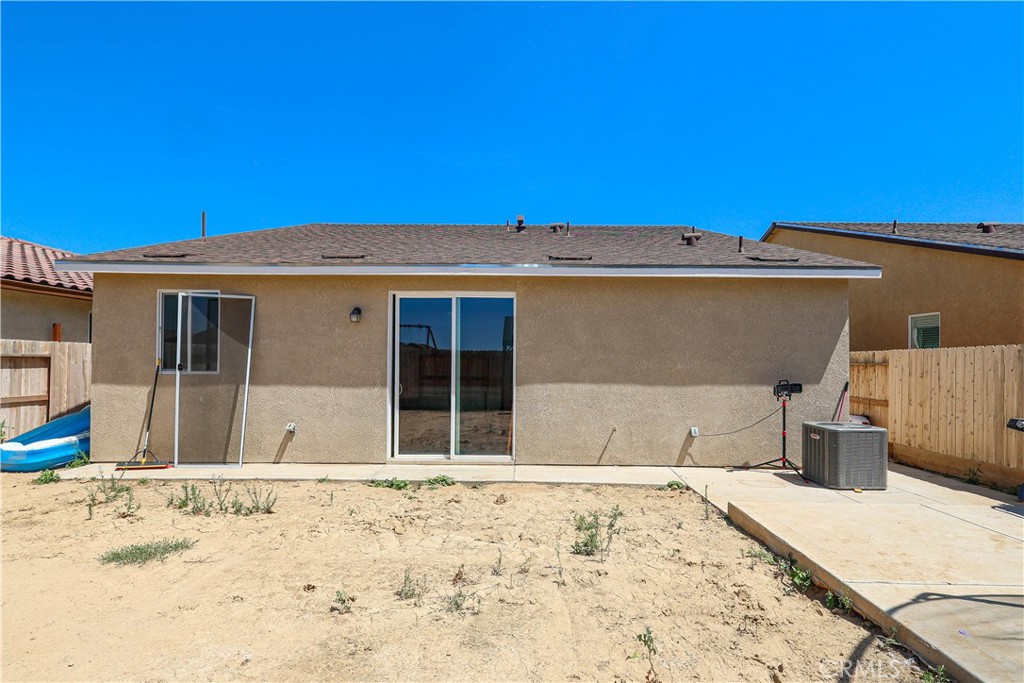 Rear of a stucco house with sliding glass doors, a concrete patio, and a mostly bare fenced yard.