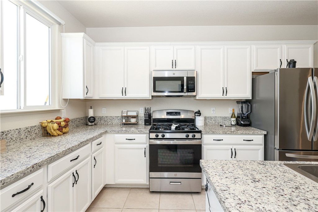 Kitchen with white cabinets, granite counters, stainless appliances, and a large window.