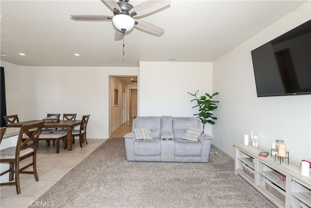 Living and dining room with a gray loveseat, large rug, wall-mounted television, and wood dining table.