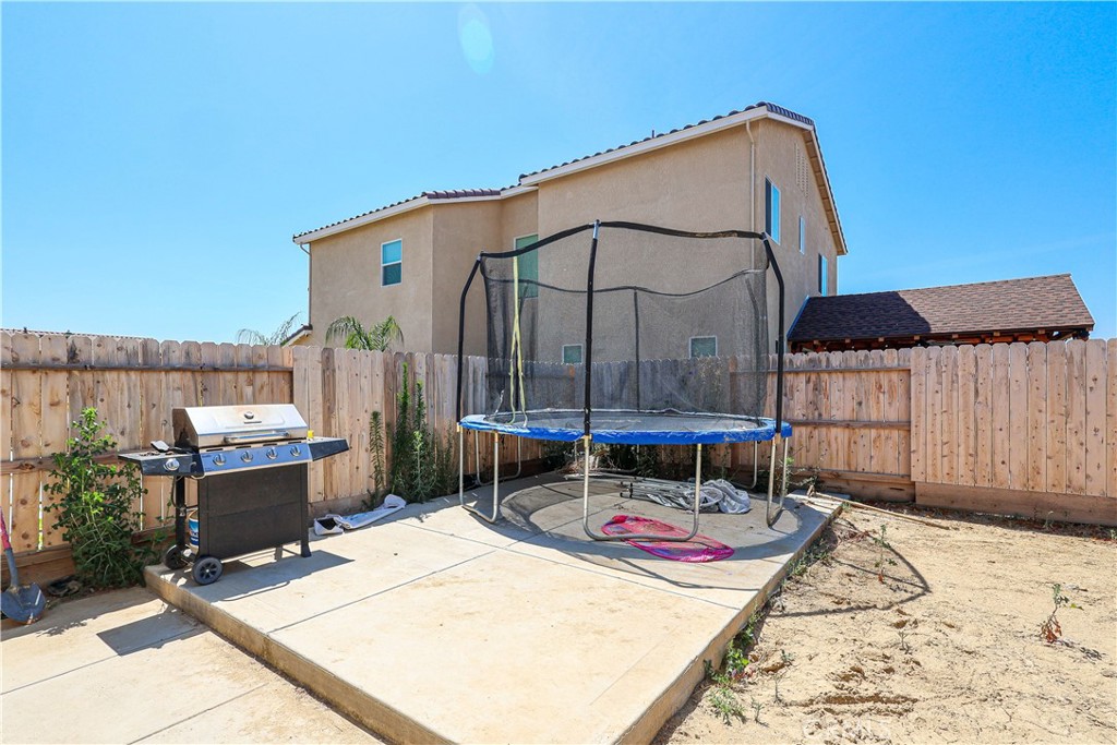 Backyard patio with a trampoline and gas grill inside a wooden fenced yard.