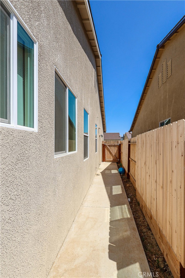 Side walkway beside a stucco home, bordered by a wooden fence and concrete path.