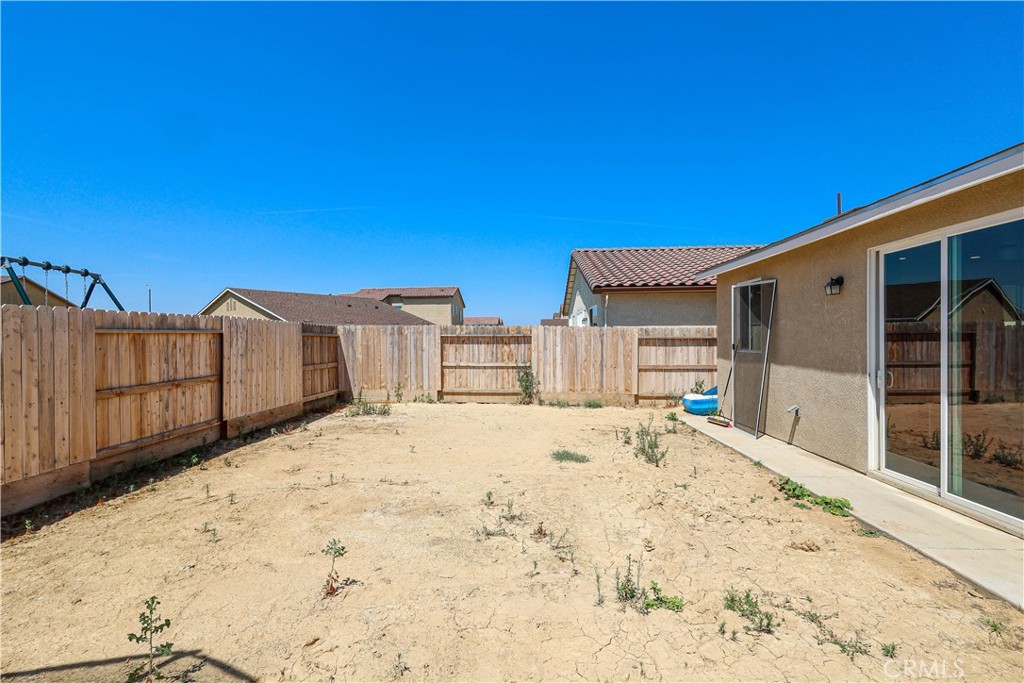 Dry, fenced backyard with a concrete patio and sliding glass doors.