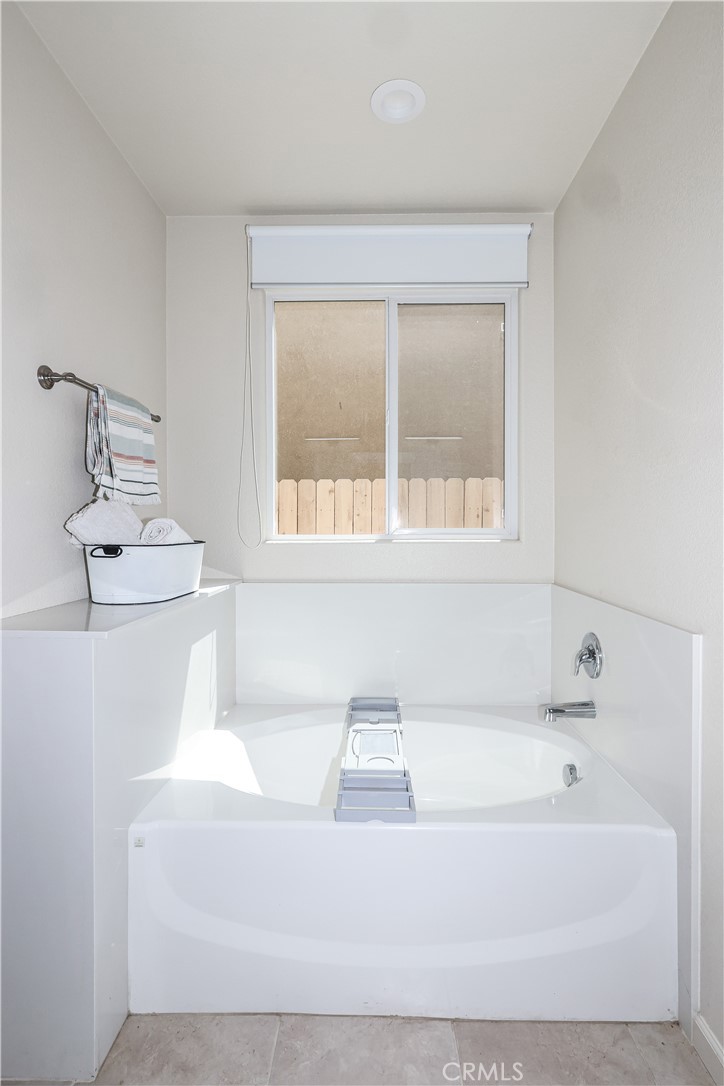 Bathroom with a large white soaking tub, central chrome faucet, and window above the tub.