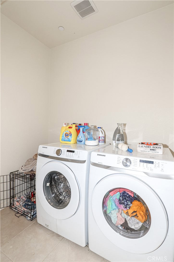 Laundry room with white front-loading washer and dryer, supplies on top and a wire laundry basket beside them.