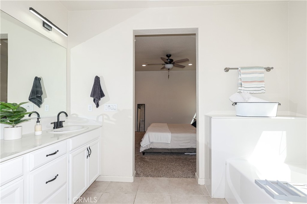 Bright bathroom with a white vanity and soaking tub, opening onto a bedroom.