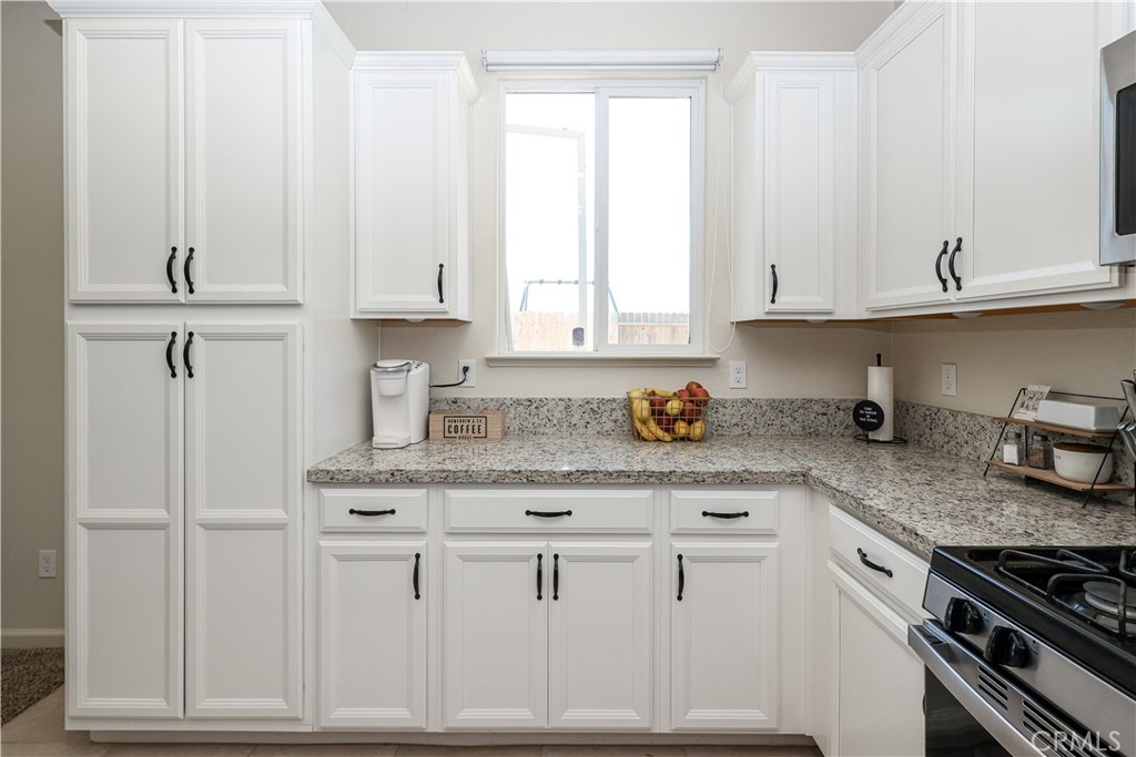 Kitchen with white paneled cabinets, speckled countertops, and a window above the counter.