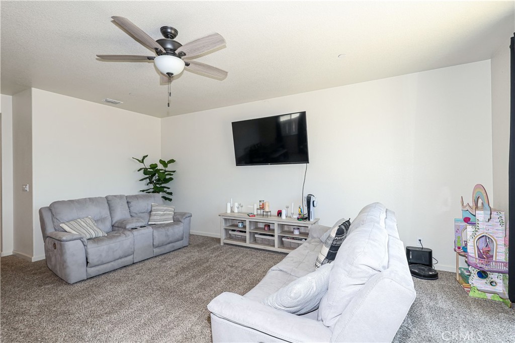 Living room with gray sofas, beige carpet, wall-mounted television, and ceiling fan.