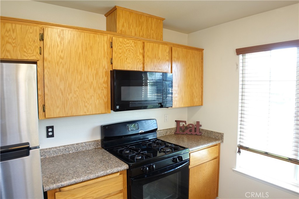 Kitchen with honey-colored cabinets, a black gas range, and an Eat sign on the counter.