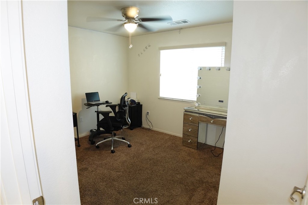 Carpeted room with a desk, office chair, lighted vanity, and ceiling fan.
