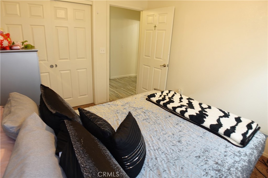 Furnished bedroom with a patterned bedspread, dark pillows, white closet doors, and an open doorway.
