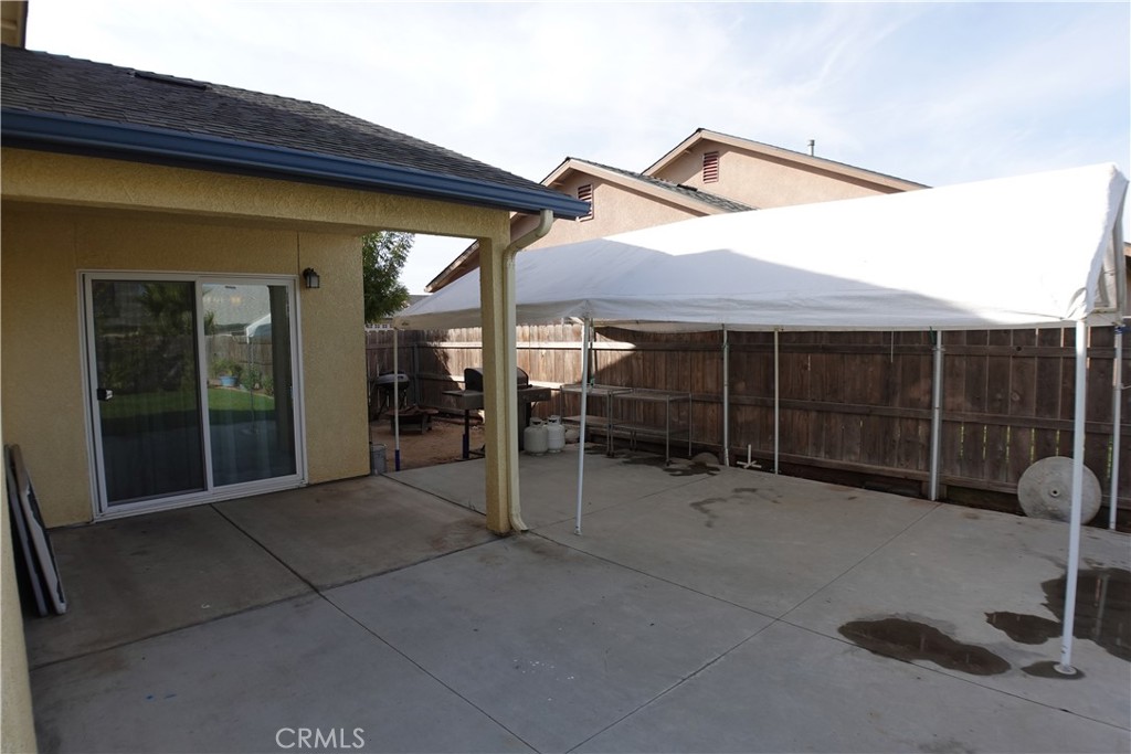 Backyard patio with a large white canopy, concrete flooring, and a wooden privacy fence.