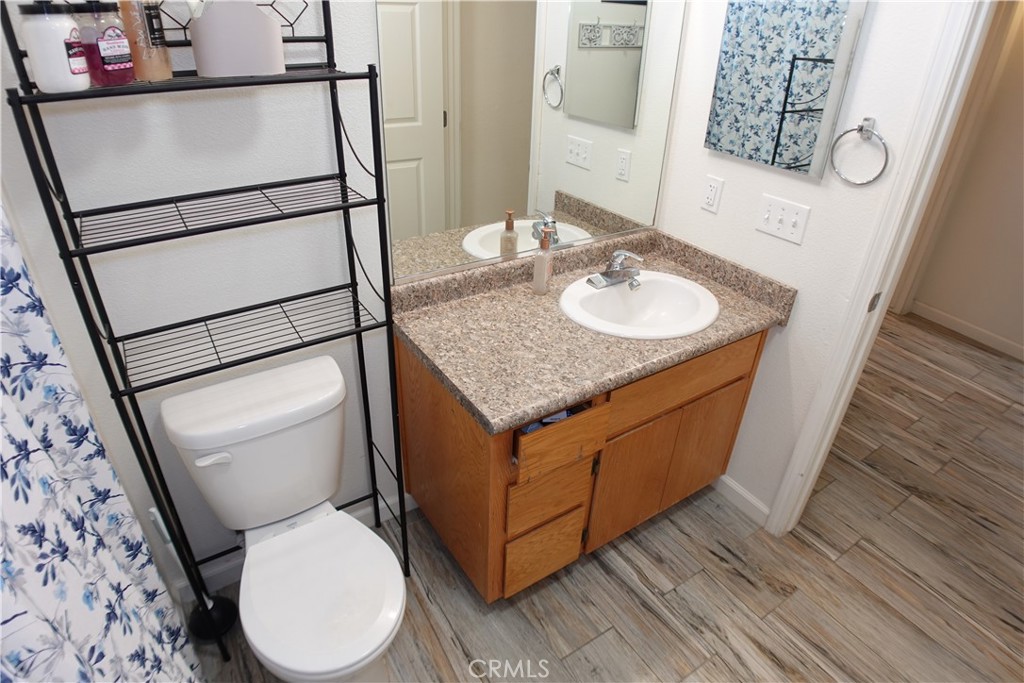 Bathroom with a wood vanity, large mirror, black shelving unit, and gray wood-look tile floor.