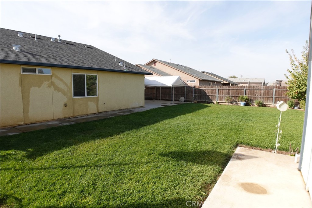 Fenced backyard with a broad green lawn, concrete patio, and white shade canopy.