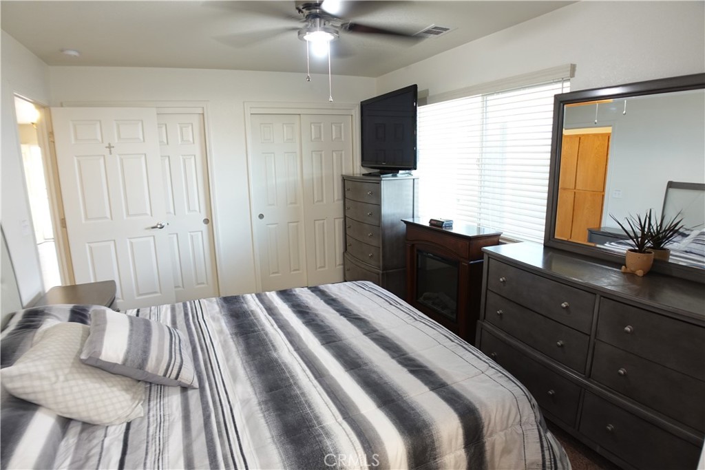 Furnished bedroom with gray-and-white striped bedding, dark wood dressers, and a ceiling fan.