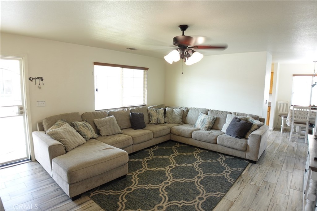 Living room with a beige sectional sofa, patterned rug, and ceiling fan; dining area visible to the right.