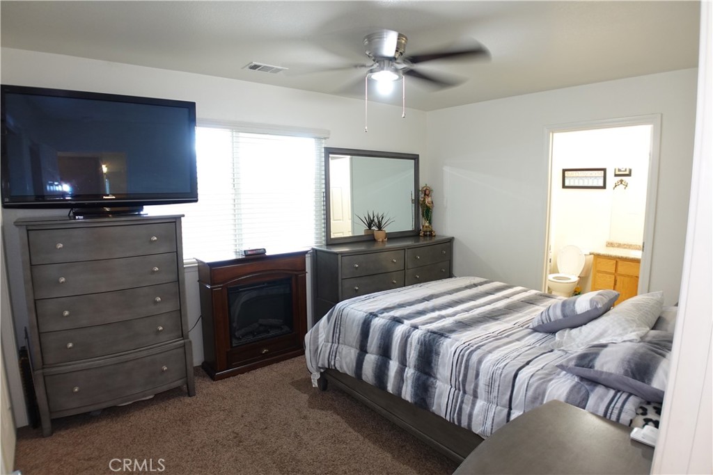 Furnished bedroom with a striped bed, matching dressers, and an adjoining bathroom doorway.