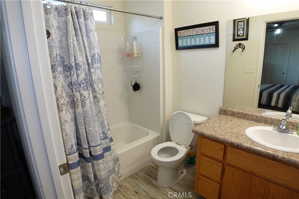Bathroom with a patterned shower curtain, bathtub, toilet, and wood vanity.