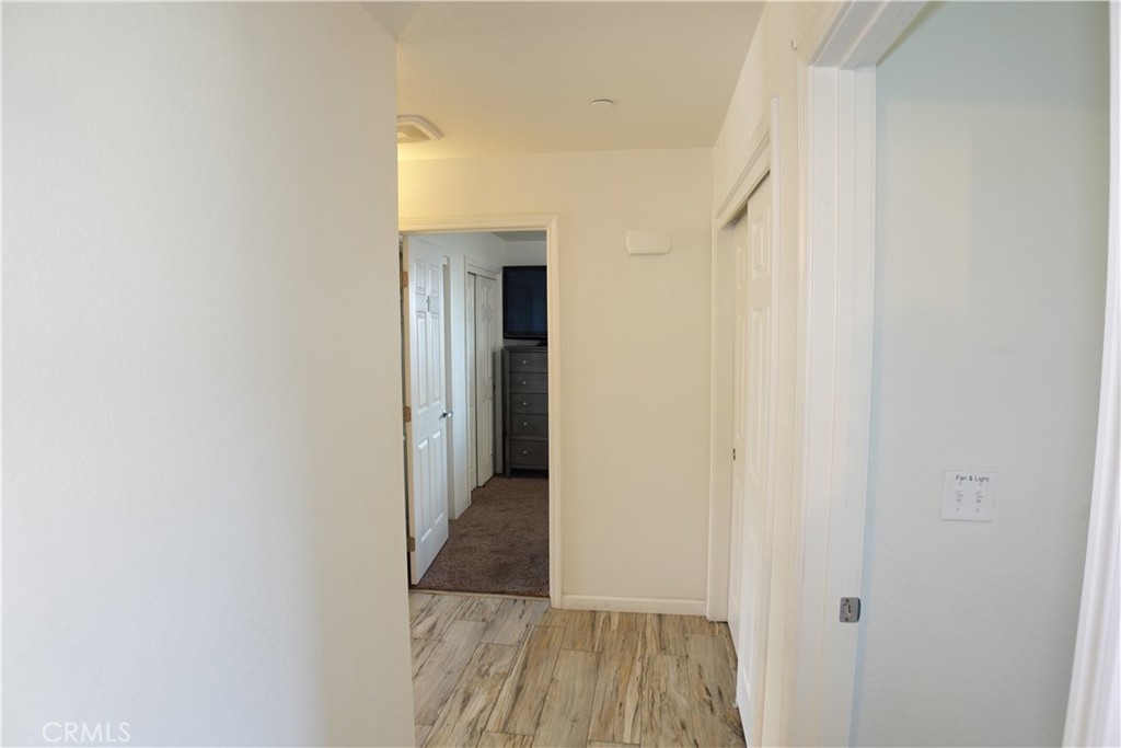 Hallway with wood-look tile flooring and white doors leading to a carpeted room.