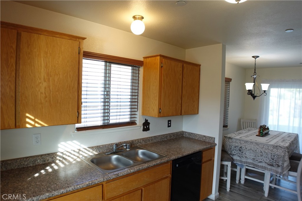 Kitchen with honey-toned cabinets, double sink, speckled counters, and an adjoining dining area.