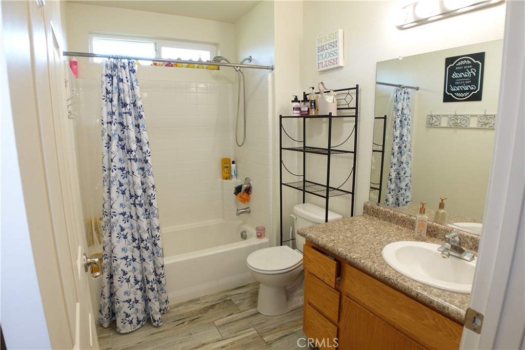 Bathroom with floral shower curtain, tub, toilet, and wood vanity with granite countertop.