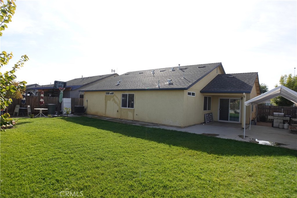 Rear of a single-story home with a wide lawn and covered patio.