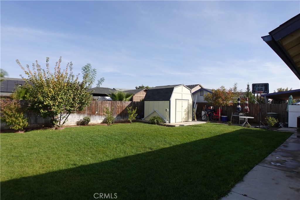 Backyard with a broad lawn, storage shed, basketball hoop, and fenced perimeter.