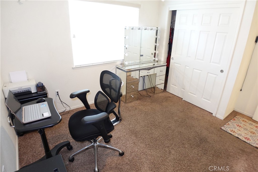 Home office with a computer desk, mesh chair, mirrored vanity, and brown carpet.