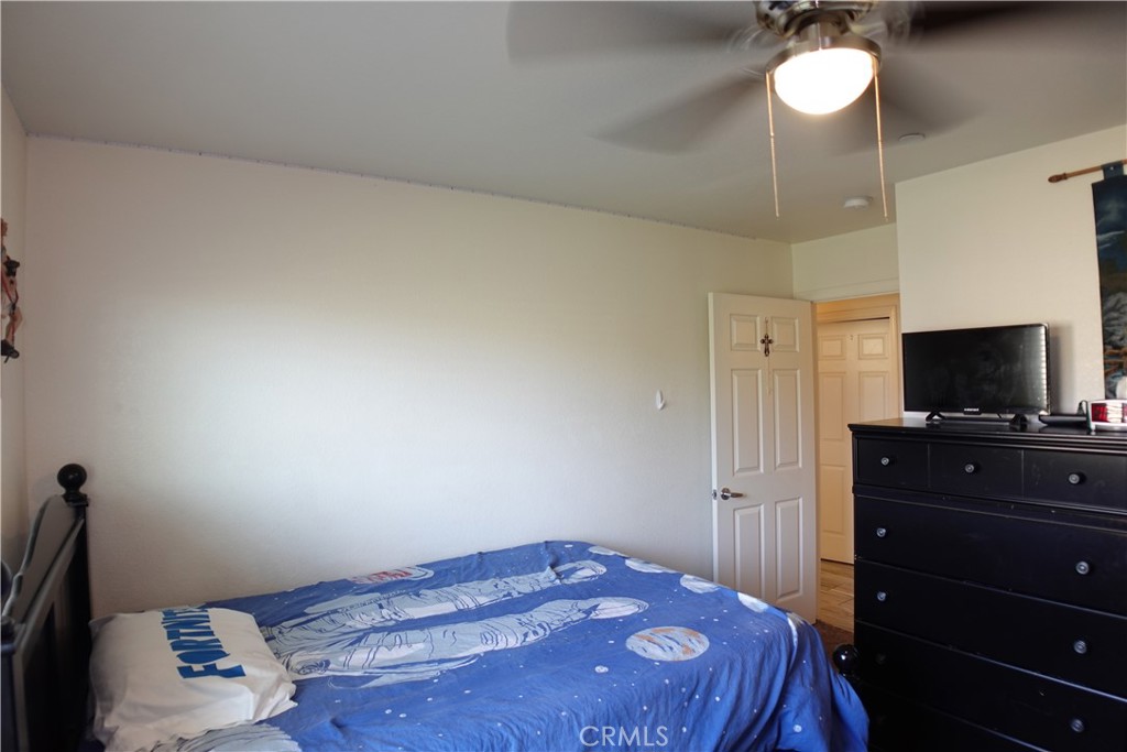 Bedroom with a blue patterned bedspread, black dresser and television, and an open doorway.