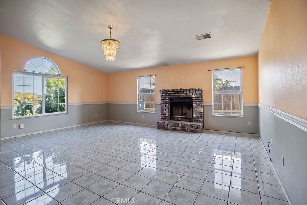 Empty living room with glossy tile floors, gray wainscoting, and a brick fireplace.