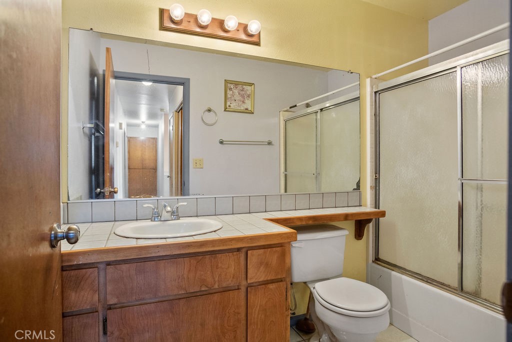 Bathroom with a wood vanity, tiled countertop, large mirror, and frosted-glass tub and shower.
