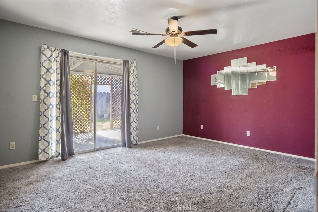 Empty living room with gray carpet, burgundy accent wall, ceiling fan, and sliding glass door.